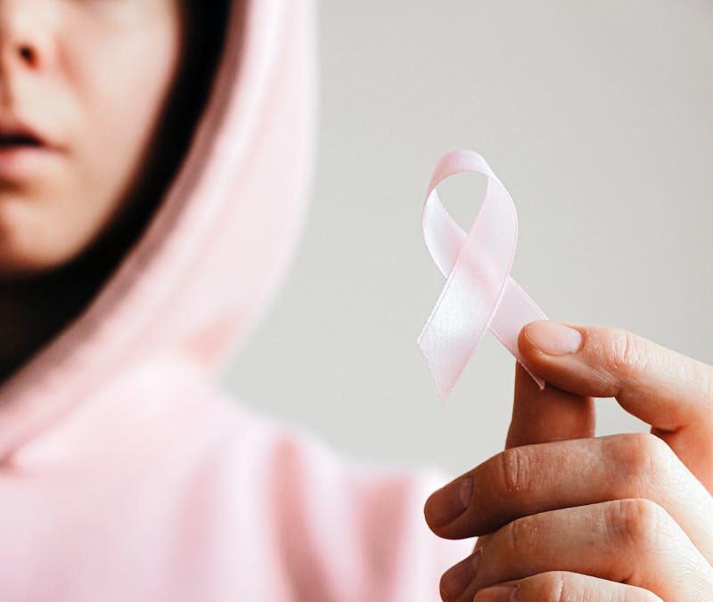 Close-up of a person holding a pink ribbon symbolizing breast cancer awareness.