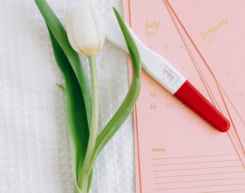 Close-up of a pregnancy test and tulip on a calendar, symbolizing new beginnings.
